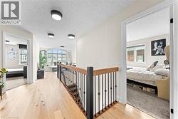 Upper-level hallway featuring light wood-finish flooring, a wood and wrought iron staircase railing, and contemporary flush-mount lighting - 
