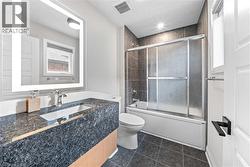Bathroom featuring a lighted vanity mirror, under-mount sink, dark stone countertop, and a tiled tub/shower combination with sliding glass doors - 