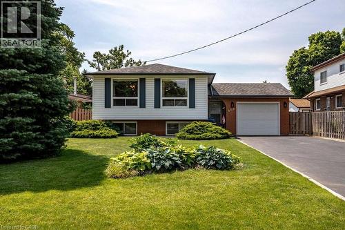 Front exterior featuring white siding with dark shutters, brick accents, an attached single-car garage, and a paved driveway - 409 Mohawk Road W, Hamilton, ON 