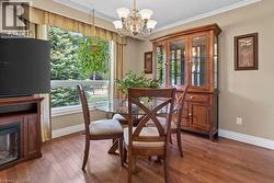 Inviting dining space featuring wood-finish flooring, a contemporary chandelier, a large window with exterior tree-line scenery, and crown molding - 