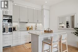 Contemporary kitchen featuring sleek white cabinetry, integrated stainless steel appliances, a generous island with a solid surface countertop, recessed lighting, and wood-finish flooring - 