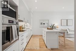 Modern kitchen featuring white cabinetry, integrated stainless steel appliances, a center island, recessed lighting, and wood-finish flooring - 