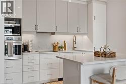 Sleek kitchen featuring light-toned cabinetry, integrated stainless steel appliances, a built-in oven, and a contemporary sink with a gooseneck faucet - 