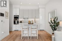 Modern kitchen featuring a central island with seating, stainless steel built-in appliances, two-tone cabinetry, and wood-finish flooring - 