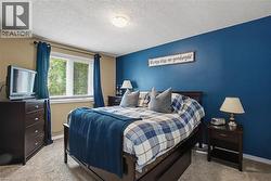 Bedroom featuring a large window with horizontal blinds, neutral wall paint, a contrasting accent wall, and textured carpeting - 