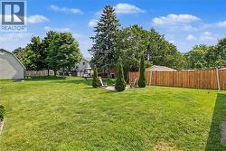 Spacious backyard featuring a lush lawn, mature trees, privacy fencing, a fire pit area, and ample room for outdoor activities - 