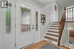 Entryway featuring a white paneled door with decorative glass, two sidelights with matching decorative glass, wood-finish flooring, and a hardwood staircase with a wood baluster - 
