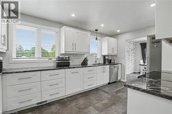 Modern kitchen featuring white shaker cabinetry, dark stone countertops, stainless steel appliances, subway tile backsplash, and dark tile flooring - 