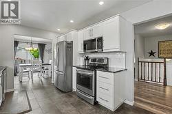Modern kitchen featuring white cabinetry, stainless steel appliances, dark countertops, and a white subway tile backsplash - 