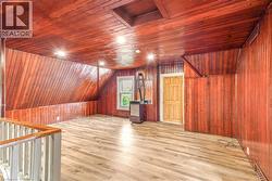 Expansive attic space featuring wood-finish flooring, wood-paneled walls and ceilings, recessed lighting, a built-in window, and a paneled door - 