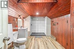 Bathroom featuring wood-finish flooring, a white vanity with a rectangular sink, a contemporary toilet, and a stand-up shower with white subway tile - 