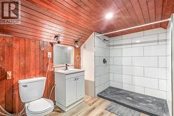 Bathroom featuring wood-finish paneling, white subway tile shower, dark shower pan, and a single-sink vanity with white cabinetry - 