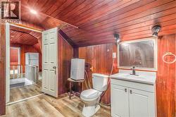 Bathroom featuring wood paneling, wood-finish flooring, a white vanity with a rectangular sink, a wall-mounted mirror, and a white toilet - 