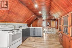Slanted wood-paneled ceilings with recessed lighting, wood-finish flooring, built-in display cabinetry, and a compact kitchen area featuring a white electric range and dark base cabinets - 