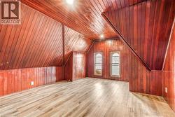Attic room with sloped wood-paneled walls and ceiling, light wood-finish flooring, and two arched windows - 