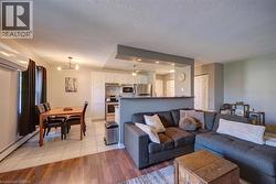Open-concept living space featuring wood-finish flooring, a kitchen with white cabinetry and stainless steel appliances, a dining area with tile flooring, and a breakfast bar - 