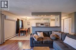 Open-concept living space featuring wood-finish flooring, a dining area with tiled flooring, and a kitchen with white cabinetry and stainless steel appliances - 