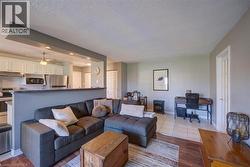 Open-concept living space featuring a kitchen with white cabinetry and stainless steel appliances, a breakfast bar, and wood-finish flooring - 