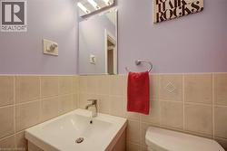 Pedestal sink with chrome faucet, light-toned tiled wainscoting, and full-width vanity mirror with integrated lighting - 