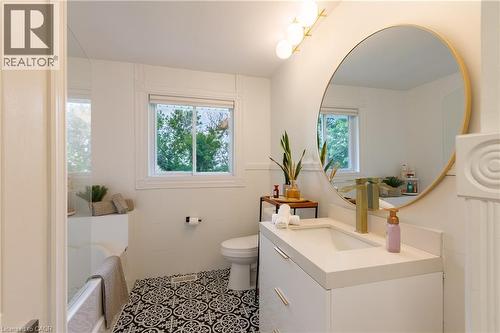 Bathroom featuring a white vanity with integrated sink, brass-finish faucet, and a large circular mirror with a brass-tone frame - 176 Riverbank Drive, Cambridge, ON 