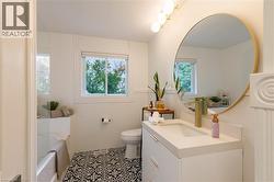 Bathroom featuring a white vanity with integrated sink, brass-finish faucet, and a large circular mirror with a brass-tone frame - 