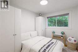 Bedroom featuring a large window with exterior tree canopy, two built-in wardrobes, and a flush-mount ceiling light fixture - 