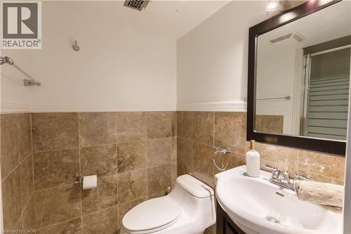 Bathroom featuring floor-to-ceiling tile, a framed mirror, and a wall-mounted sink - 176 Riverbank Drive, Cambridge, ON 