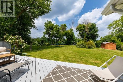 Spacious rear yard with a bright green lawn, mature trees, a wooden storage shed, and a grey plank deck - 176 Riverbank Drive, Cambridge, ON 