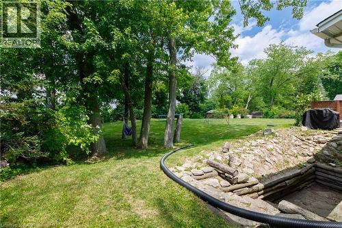 Expansive lawn area featuring mature trees and a stone-lined excavation - 176 Riverbank Drive, Cambridge, ON 