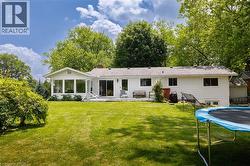 Expansive rear yard featuring a manicured lawn, mature trees, and a sunroom with large windows - 