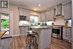 Kitchen featuring wood-finish flooring, light grey cabinetry, stone countertops, a subway tile backsplash, and stainless steel appliances - 
