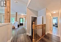 Hallway featuring wood-finish flooring, light-toned wall paint, and a wood baluster staircase - 
