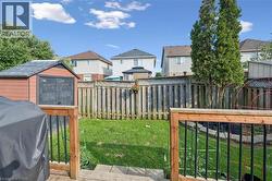 Expansive backyard featuring a wood deck with black metal railings, a manicured lawn, a wooden storage shed, and a tall privacy fence - 