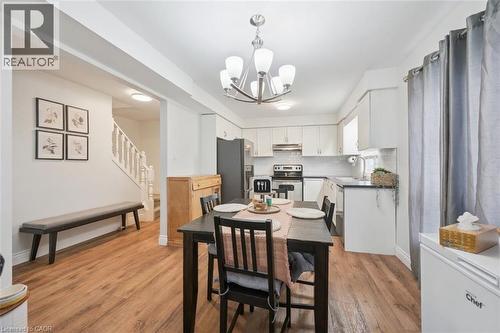 Dining area featuring wood-finish flooring, a contemporary chandelier, and an open layout to a kitchen with white cabinetry, dark countertops, and a subway tile backsplash - 765 Angler Way, Waterloo, ON 