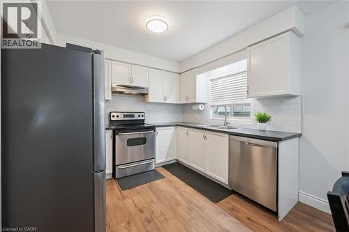 Modern kitchen featuring white cabinetry, dark countertops, wood-finish flooring, a stainless steel range, and a stainless steel dishwasher - 765 Angler Way, Waterloo, ON 