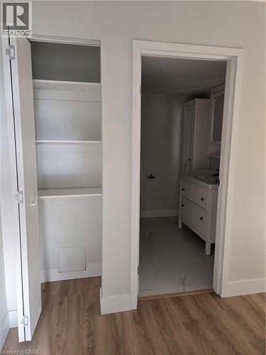 Interior hallway featuring wood-finish flooring, a built-in linen closet with shelving, and a doorway opening to a bathroom with a white vanity and tiled flooring - 3085 Kingsway Drive Unit# 21, Kitchener, ON 