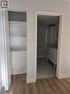 Interior hallway featuring wood-finish flooring, a built-in linen closet with shelving, and a doorway opening to a bathroom with a white vanity and tiled flooring - 