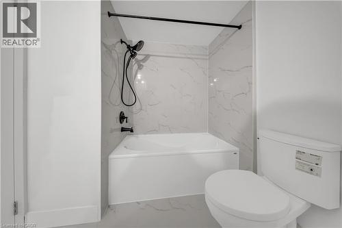 Bathroom featuring a white bathtub, white toilet, and white tile surround with gray veining - 3085 Kingsway Drive Unit# 21, Kitchener, ON 