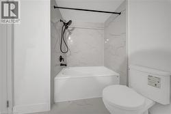 Bathroom featuring a white bathtub, white toilet, and white tile surround with gray veining - 
