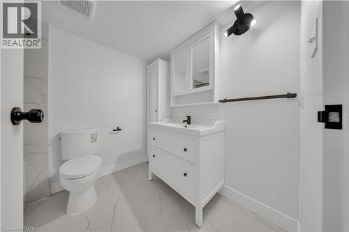 Bathroom featuring a white vanity with integrated sink, coordinating wall cabinet, white toilet, and marble-look tile flooring - 3085 Kingsway Drive Unit# 21, Kitchener, ON 