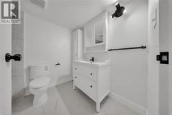 Bathroom featuring a white vanity with integrated sink, coordinating wall cabinet, white toilet, and marble-look tile flooring - 