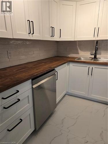 Kitchen featuring white shaker-style cabinetry with matte black hardware, wood-finish countertops, stainless steel dishwasher, and a rectangular undermount sink with a matte black faucet - 3085 Kingsway Drive Unit# 21, Kitchener, ON 