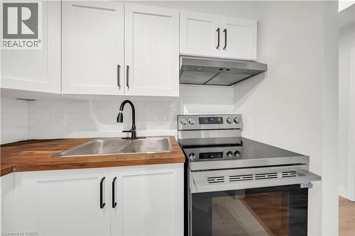 Modern kitchen featuring white shaker cabinetry with dark hardware, a stainless steel double basin sink with a black gooseneck faucet, butcher block countertops, white subway tile backsplash, and a st - 3085 Kingsway Drive Unit# 21, Kitchener, ON 