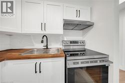 Modern kitchen featuring white shaker cabinetry with dark hardware, a stainless steel double basin sink with a black gooseneck faucet, butcher block countertops, white subway tile backsplash, and a st - 