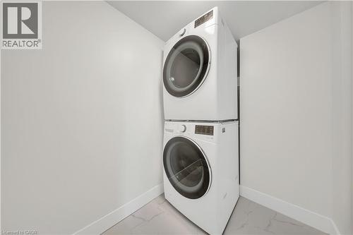 Dedicated laundry area featuring a stacked washer and dryer, contemporary white baseboards, and light-toned tile flooring - 3085 Kingsway Drive Unit# 21, Kitchener, ON 