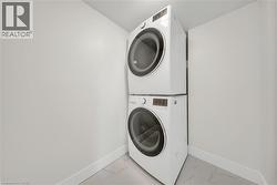 Dedicated laundry area featuring a stacked washer and dryer, contemporary white baseboards, and light-toned tile flooring - 