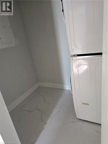 Laundry area featuring white stacked appliances, white baseboards, and white tile flooring with grey veining - 3085 Kingsway Drive Unit# 21, Kitchener, ON 