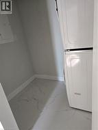 Laundry area featuring white stacked appliances, white baseboards, and white tile flooring with grey veining - 