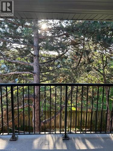 Outdoor balcony featuring a black metal railing and concrete flooring, overlooking mature trees and a wooden privacy fence - 3085 Kingsway Drive Unit# 21, Kitchener, ON 