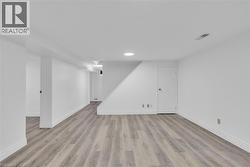 Spacious room featuring wood-finish flooring, white walls, recessed lighting, and a white door with a brass-finish knob - 